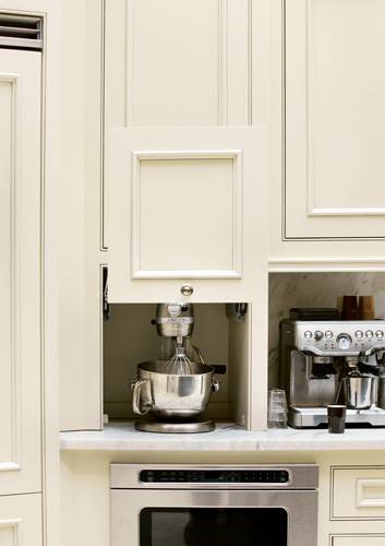 Beautiful kitchen with Calacatta Fantastico honed marble countertops and seamless backsplash. The marble pairs with creamy white cabinets and polished nickel hardware. A versatile appliance cabinet with slide-up cabinet front hides a silver KitchenAid Mixer. Beside the mixer stands a cappuccino maker and below, a built-in stainless steel microwave.