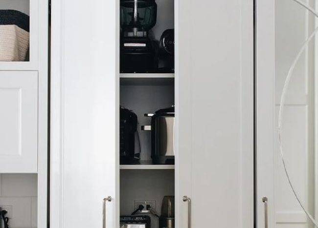 Beautiful white kitchen boasts a white cabinet fitted with white shelves and dedicated to small kitchen appliances.