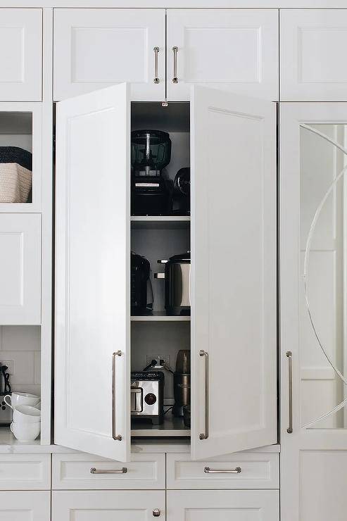 Beautiful white kitchen boasts a white cabinet fitted with white shelves and dedicated to small kitchen appliances.