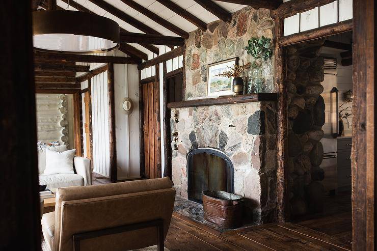 Welcoming log cabin boasts a rustic stone fireplace fitted with a styled rustic wood mantel mounted beneath a two-toned vaulted plank ceiling.