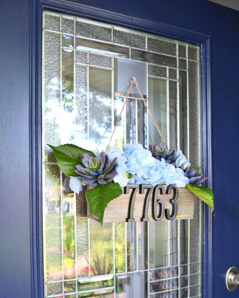 decorative planter box with faux flowers house numbers hanging from blue front door