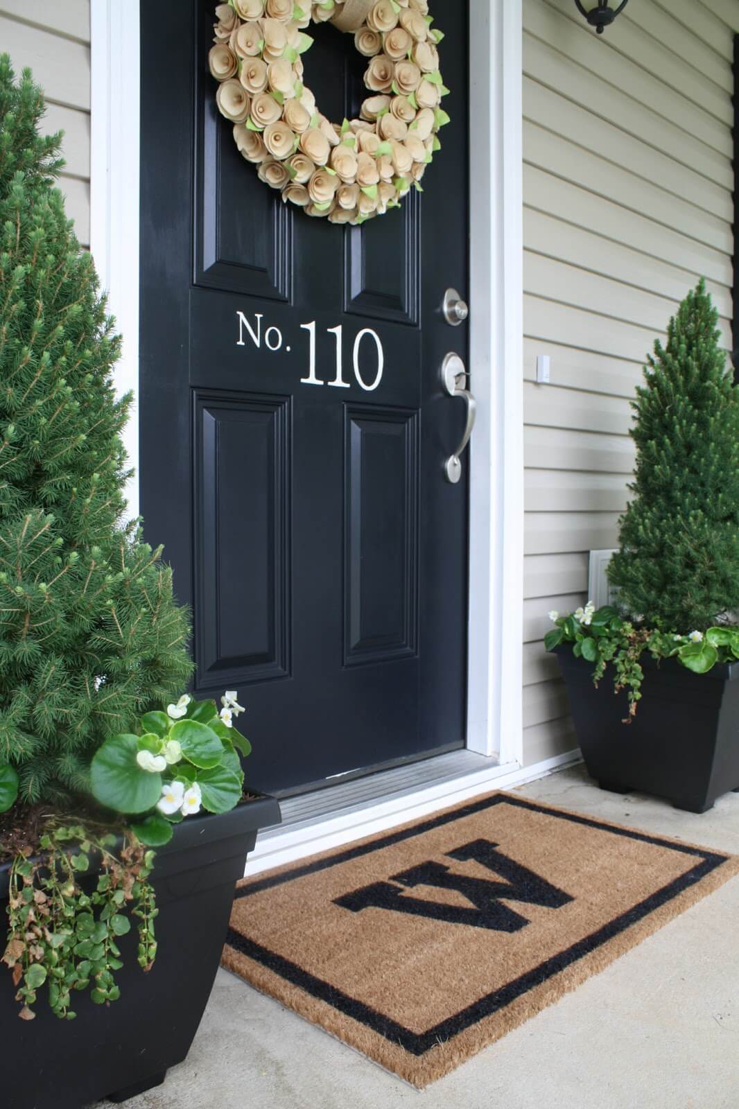 black front door with white vinyl decal numbers cream wreath w monogram door mat green trees