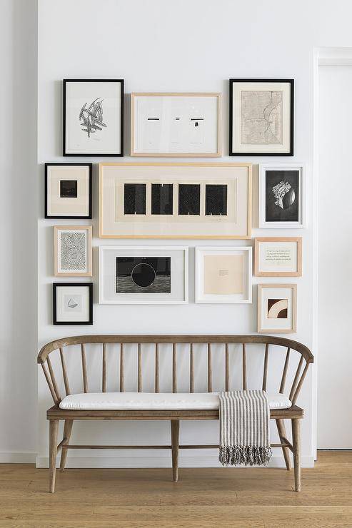 Foyer designed with a curved wooden spindle bench dressed with a gray stripe throw blanket and a white cushion. Wall art frames decorate the entry wall with a charming display.