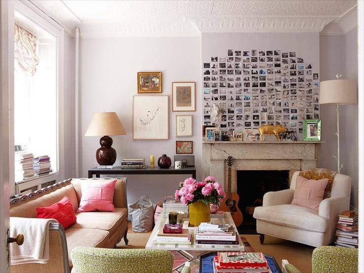 Eclectic living room design with white branch floor lamp, white sofa, black glass console table, maroon gourd lamp, pink pillows, Polaroid photo wall gallery, marble fireplace and soft lilac walls paint color.