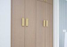 Brass hexagon hardware complements stacked floor-to-ceiling brown oak hallway cabinets.