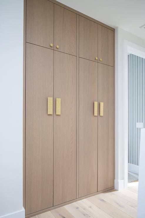 Brass hexagon hardware complements stacked floor-to-ceiling brown oak hallway cabinets.