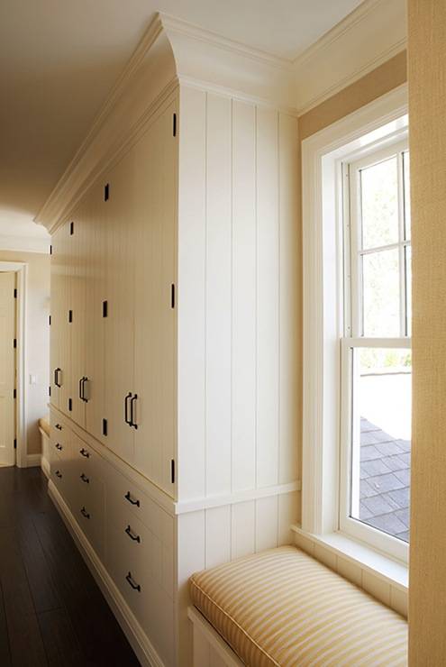 Beautiful light filled hallway with ceiling height built-in closets finished with crown molding and iron hardware. The linen closets area flanked by a pair of built-in window seats with striped seat cushions. Dark hardwood floors finish the space.