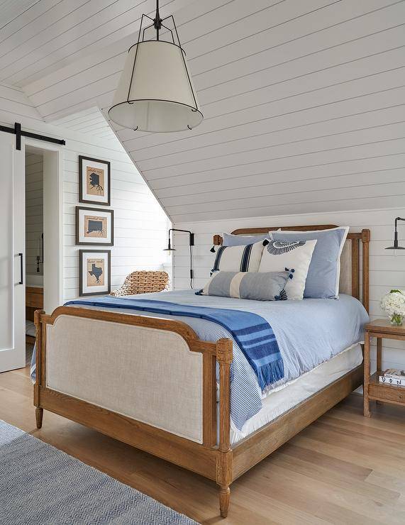 French wooden and fabric bed in a cottage bedroom with shiplap walls and oak nightstands fitted with hanging black industrial shade lamps.