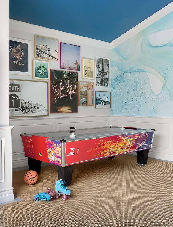 Game room features an airy hockey table in a room decorated with wainscoting walls and an ocean blue ceiling. Wall art decorates the walls with various frames, colors, and themes.