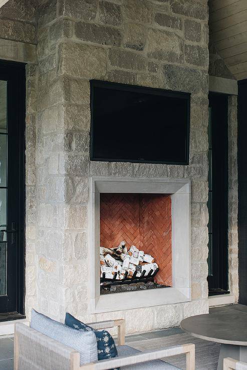 A beautifully appointed covered patio boasts a gray stone fireplace fitted with a TV niche.