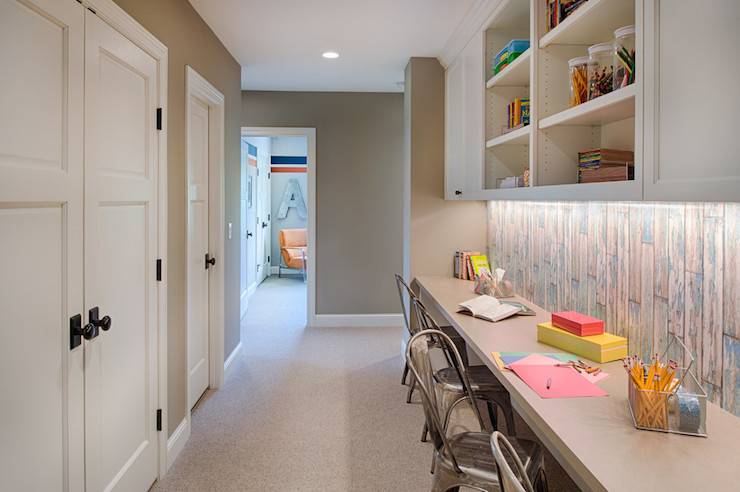 Hallway homework station with built-in upper cabinets with open shelving over a weathered plank effect backsplash alongside a wall to wall taupe counter lined with Tolix chairs atop beige wall to wall carpeting.