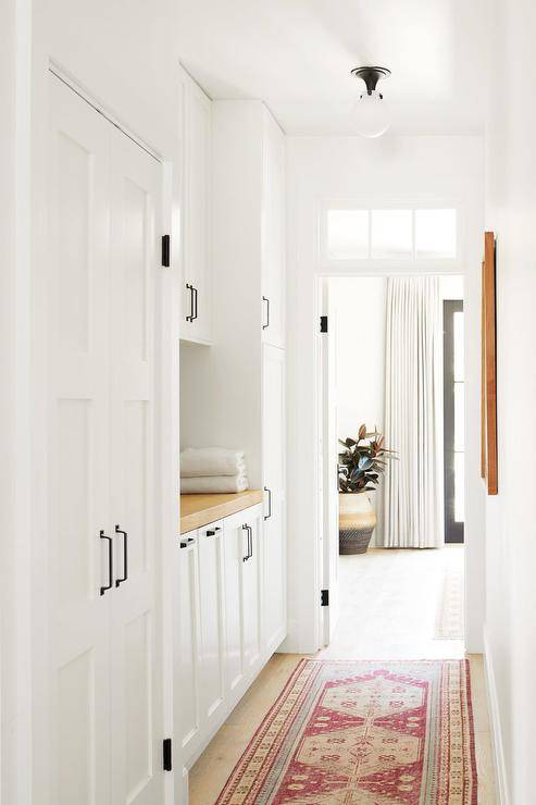 Hallway laundry room designed with a butcher block countertop and white cabinets fitted with oil rubbed bronze hardware.