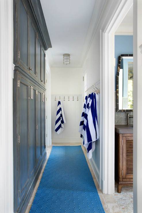 Beachy hallway with built-in dark stained mud room cabinets across from 3/4 tongue and groove paneled walls lined with coat hooks adorned with navy striped towels over tiled floors layered with a Dash and Albert Diamond Rug Runner.