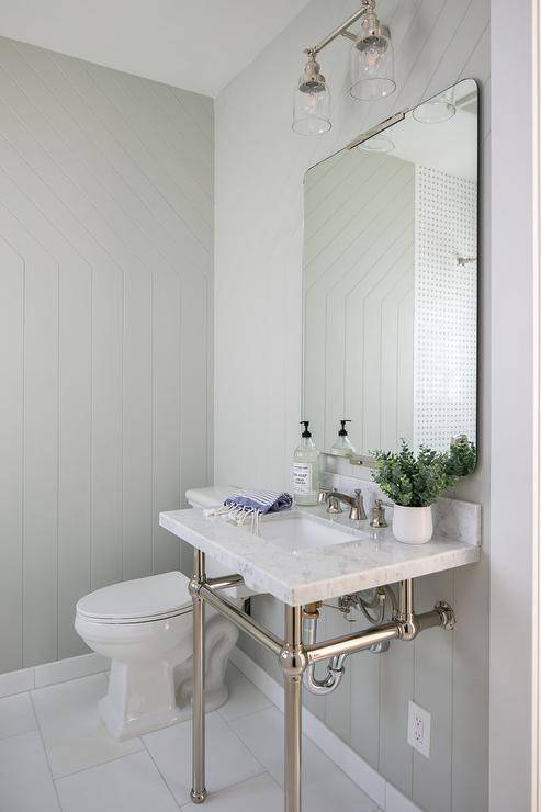 Bathroom designed with a vertical gray shiplap wall trim and a nickel and marble washstand finished with a curved nickel mirror.