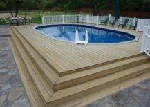 large wood deck built around a rectangle above ground pool patio chairs and white fence