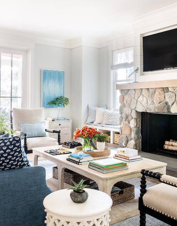 Welcoming living room features a TV fixed in a shiplap niche over a rustic gray stone fireplace. A light stained wooden coffee table sits on a blue rug in front of a blue sofa.