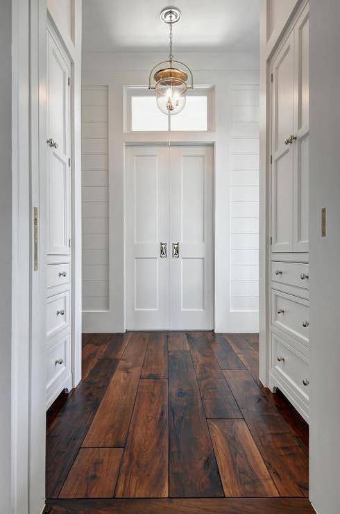 Beautiful natural tung oiled solid walnut plank floors illuminated by a polished nickel Urban Electric Dover bell light white walls lined with inset, built-in white shaker cabinets fitted with polished nickel knobs lead to white hide away doors positioned under a small transom window flanked by white board and batten trimmed shiplap walls. This symmetrically laid out master bedroom has a “Her Master Bath”, along with “Her Closet and Dressing room, on one side of the room. The “His Master Bath” and "His Closet / Dressing Room are on the opposite side of the room.