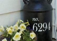 black milk jug with house numbers painted on it next to planter on porch