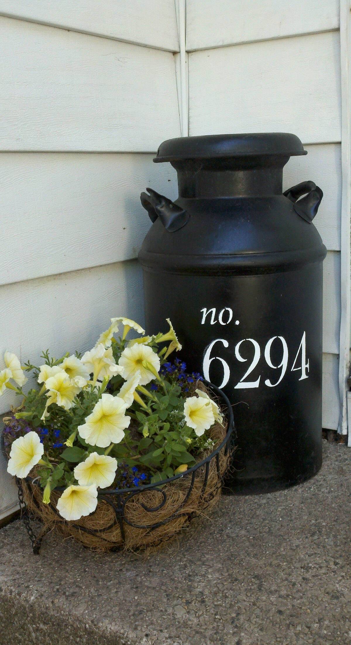 black milk jug with house numbers painted on it next to planter on porch