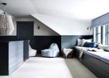 White, black, and blue attic playroom boasts a black shiplap built-in window seat topped with light gray cushions and pillows placed beneath a window dressed in a light blue roman shade. The roman shade matches blue bean bags placed in front of a wall half clad in black shiplap trim.