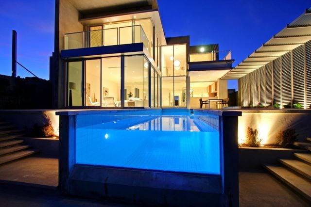 pool without wall lit up at night behind modern house with lots of windows