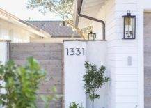 Exterior home features modern steel house numbers displayed on a white finished wooden house gate. Winding stone pavers sets a surface toward the wooden gate into a finished backyard.