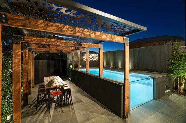 open edge above ground pool at night on patio with pergola