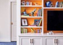 Orange shiplap is on the back of white built in shelves over blue carpet.