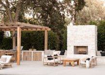 A white stone outdoor fireplace is flanked by built-in benches topped with black and gray pillows.