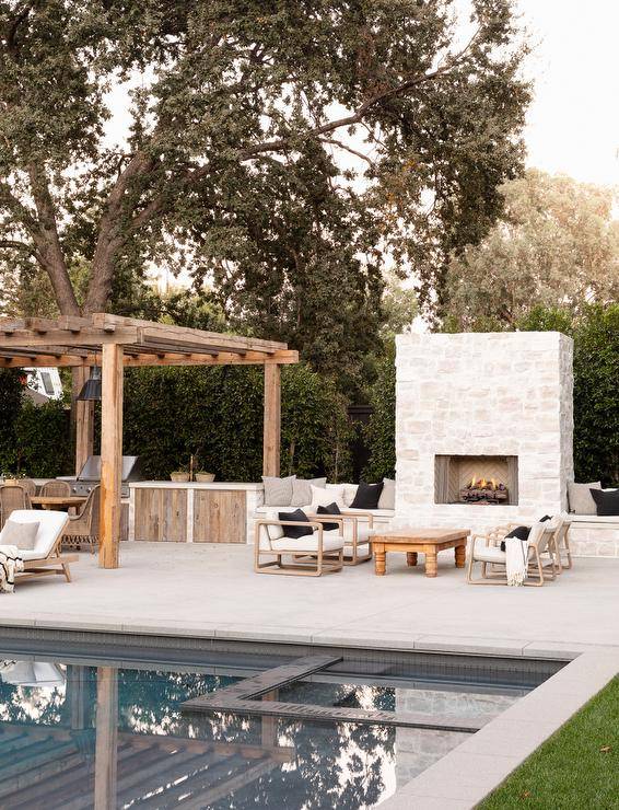 A white stone outdoor fireplace is flanked by built-in benches topped with black and gray pillows.