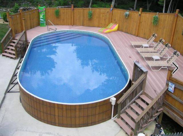 oval wood frame pool with deck built on one side on cement slab with lounge chairs on deck