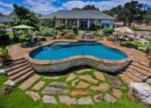 peanut shape above ground pool with rock wall steps and behind house
