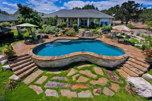 peanut shape above ground pool with rock wall steps and behind house