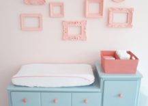Pink and aqua blue nursery with changing table painted blue, Sherwin Williams Interesting Aqua, adorned with pink hardware below walls painted pink, Sherwin Williams Armour Pink, accented with a gallery wall of empty frames painted Sherwin Williams Hopeful.