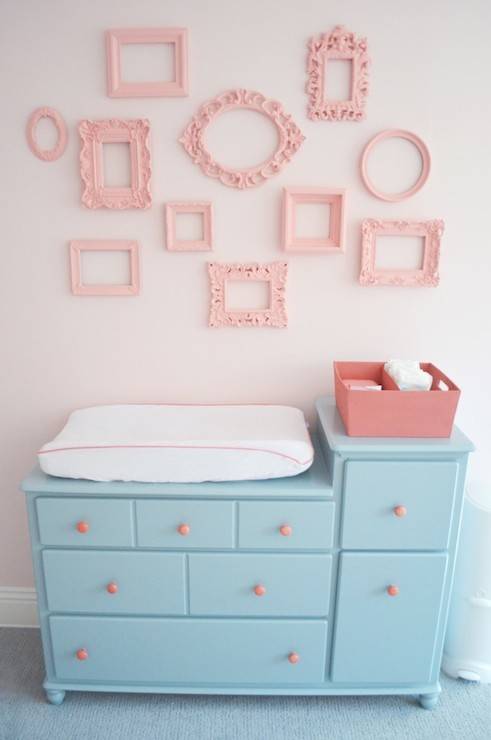 Pink and aqua blue nursery with changing table painted blue, Sherwin Williams Interesting Aqua, adorned with pink hardware below walls painted pink, Sherwin Williams Armour Pink, accented with a collage wall of empty frames painted Sherwin Williams Hopeful.