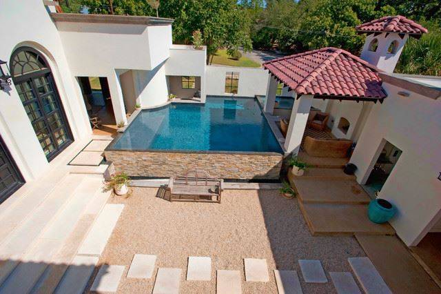 above ground pool built into patio with stone wall red roof stucco white house