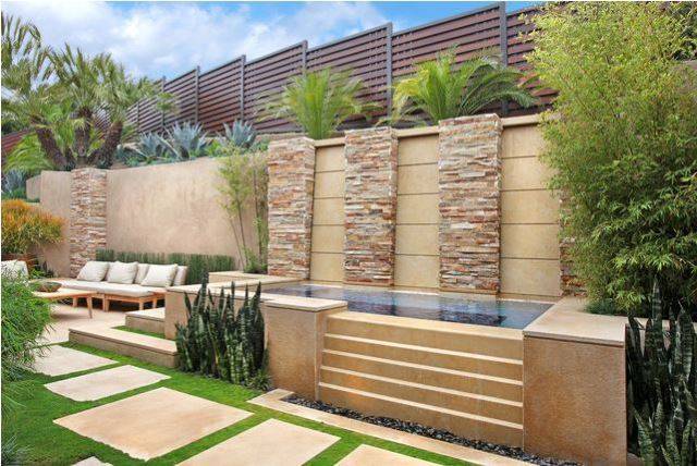 rectangle above ground pool with steps stone wall feature behind on concrete paver patio with grass