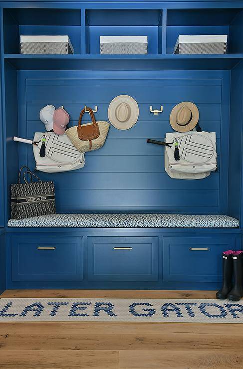 Mudroom features a blue shiplap built in bench with drawers and blue cushion and a later gator rug.