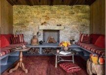 Welcoming outdoor lounge boasts a stone fireplace and a red rug framed by a u-shaped concrete bench topped with red striped cushions and red pillows.