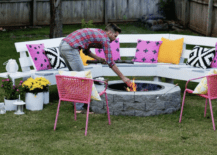 stone fire pit with benches and pink black and yellow pillows pink chairs man feeding fire with wood