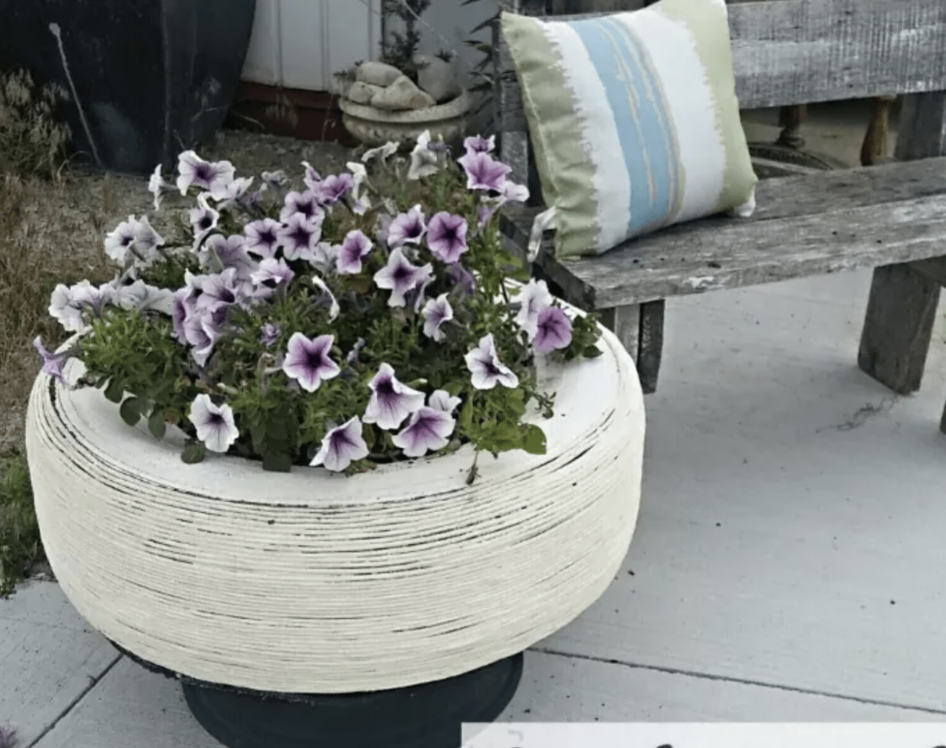 white jute wrapped tire planter with pansies on patio