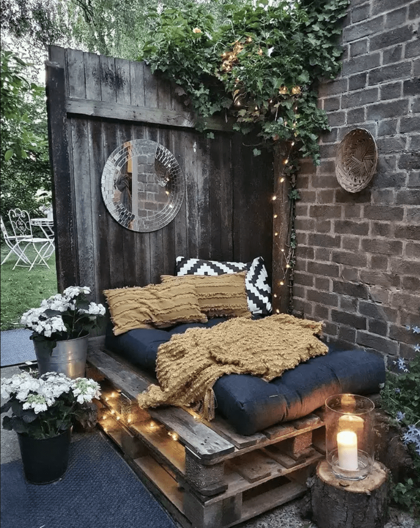 napping nook in backyard made out of pallets along fence and brick wall