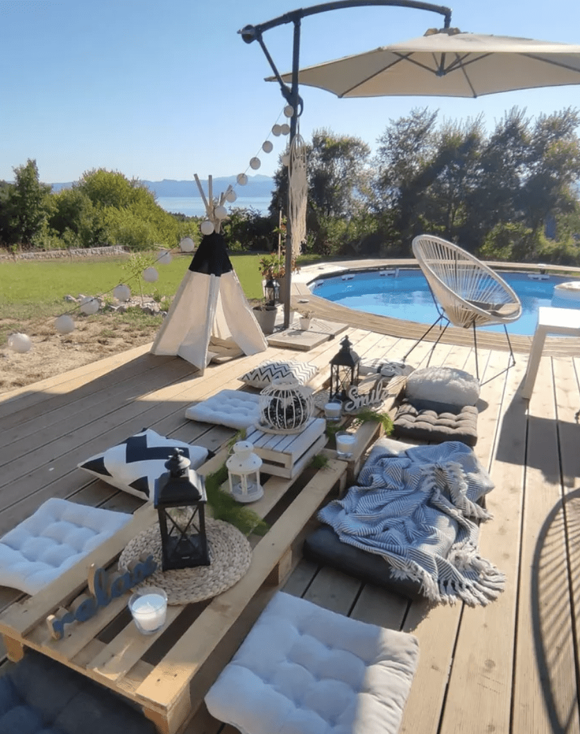 above ground pool with tufted cushion floor seating and dining table white patio umbrella on a stand and outdoor kids teepee