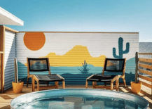 colorful backdrop behind a stock tank pool on a patio with two black lounge chairs