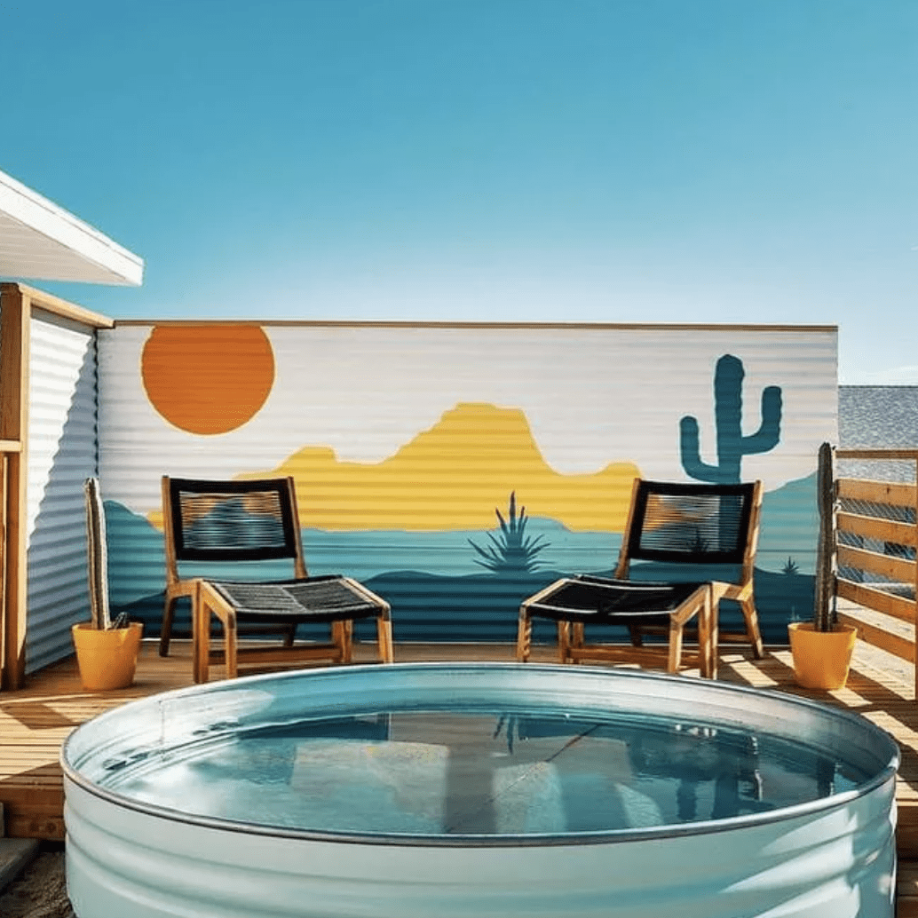 colorful backdrop behind a stock tank pool on a patio with two black lounge chairs
