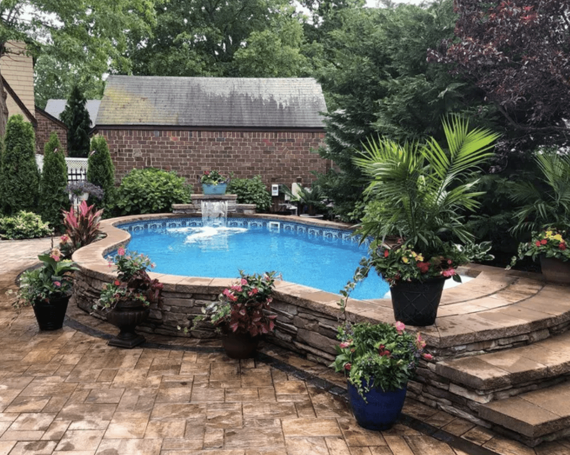 backyard above ground pool framed in with slate stone wall steps palms and planters