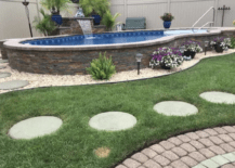 stone wall framed above ground pool surrounded by grass and paver walkway
