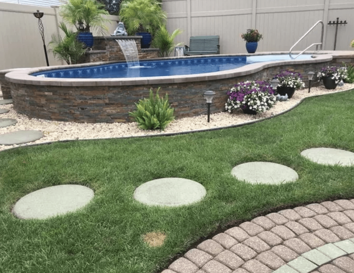 stone wall framed above ground pool surrounded by grass and paver walkway