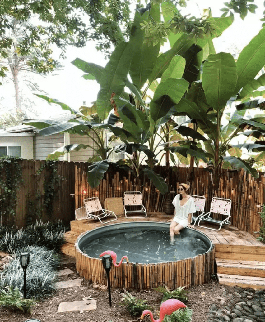 stock tank pool wrapped with rustic sticks a woman sitting on the side with her feet in plastic pink flamingos