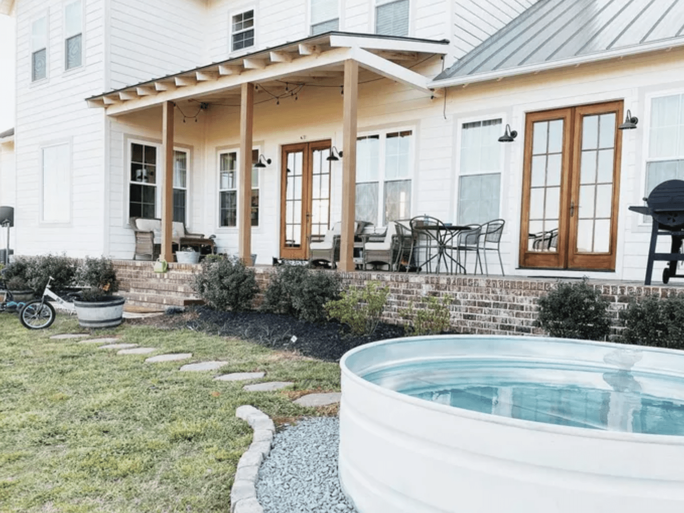 white stock tank pool in front of a white farmhouse with wood door